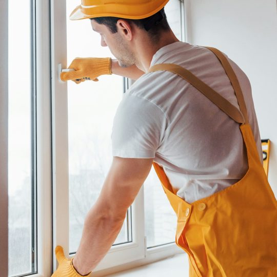 Handyman in yellow uniform installs new window. House renovation conception